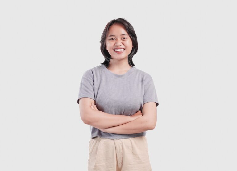 Confident young Asian woman standing with arms folded and smiling at camera